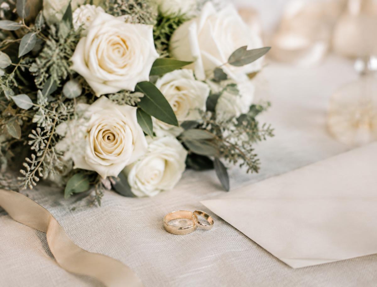 Ivory rose bouquet with two gold wedding rings on linen
